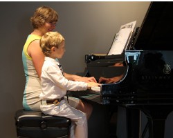 Piano student plays duet with piano teacher at music recital
